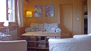 Una stanza accogliente con pareti in legno e un tavolo anch'esso in legno. C'è un divano con cuscini decorati e una lampada sul tavolo.