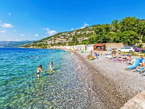 A beach with clear shallow waters, pebbly shore, and a hillside with buildings. - Nice apartment for 5 people with WIFI, A/C, TV and terrace (Senj)
