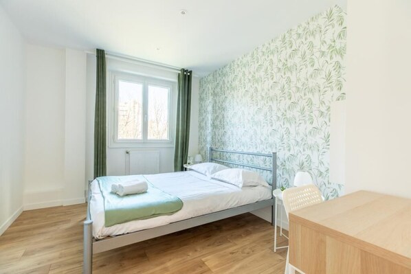 Cozy retreat with a comfortable metal bed, a wooden desk, and a chair, set against a leafy wallpaper backdrop.