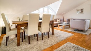 Ein modernes Schlafzimmer im Loft-Stil mit schrägen Wänden, einem Essbereich mit Holztisch und Stühlen, einem Sofa und einem kleinen Couchtisch.