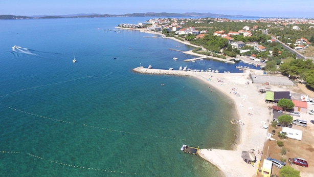 Luftaufnahme einer Küstenstadt mit klarem, blauem Wasser, einem Sandstrand und Wohngebäuden.