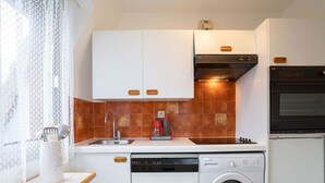 Una cucina compatta con mobili bianchi, lavastoviglie, lavatrice e forno.