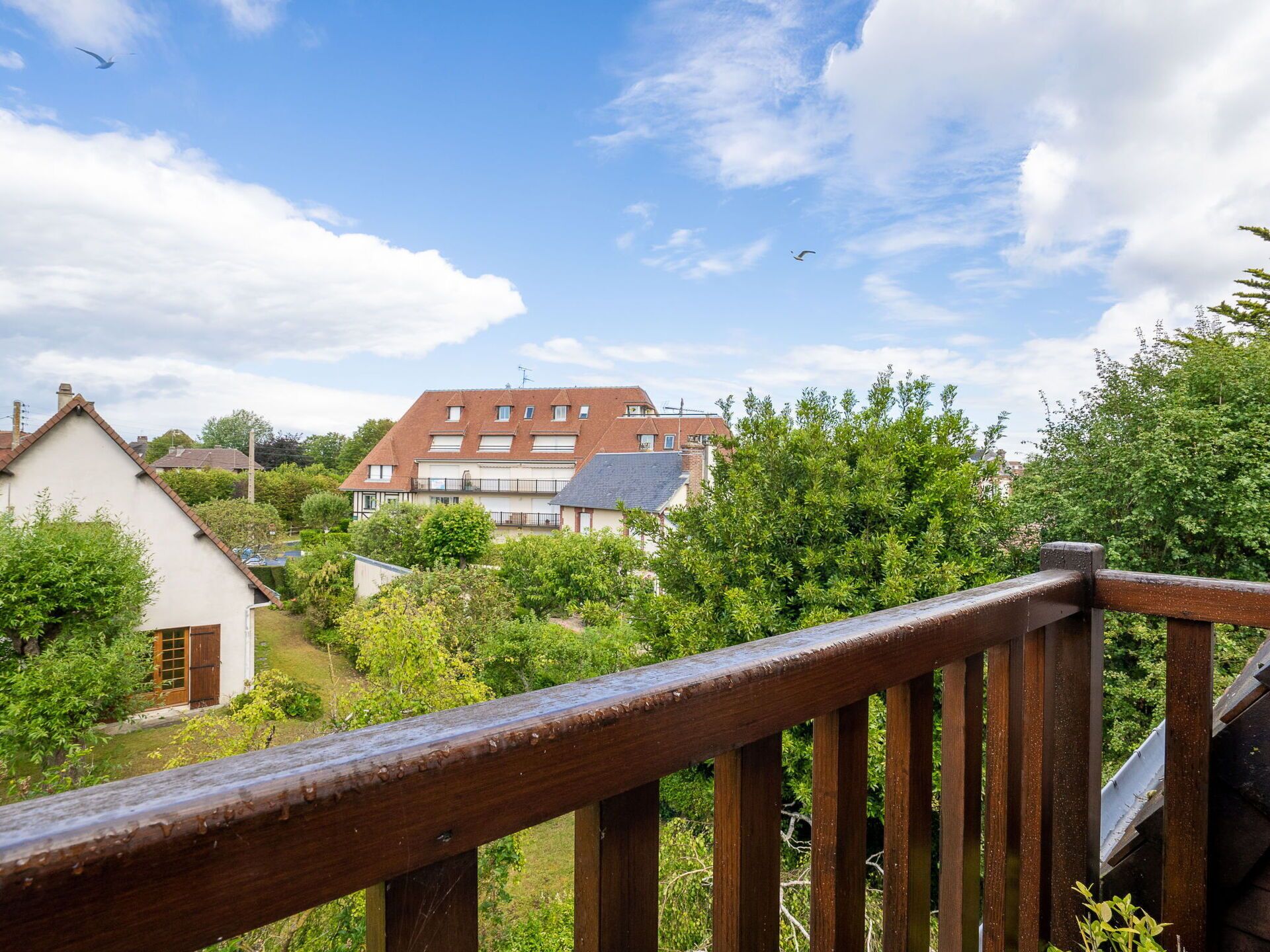 A residential area with a two-story house, a wooden fence, and lush greenery.