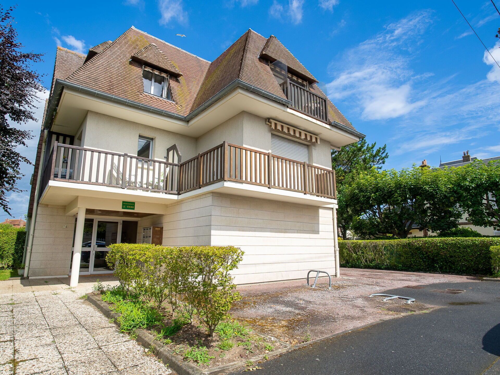 A two-story building with a balcony on the ground floor and a small garden area in front.