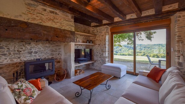 Un interior rústico con paredes de piedra, techo de madera, televisión, sofá y vistas al exterior.