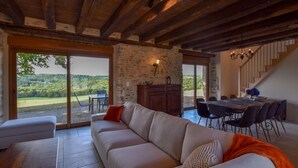 Amplia sala de estar con pared de piedra, techo de madera y un gran ventanal corredera que da a una terraza.