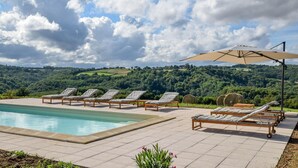 Zona junto a la piscina con sillas de descanso y una sombrilla grande, con vistas a un paisaje pintoresco.