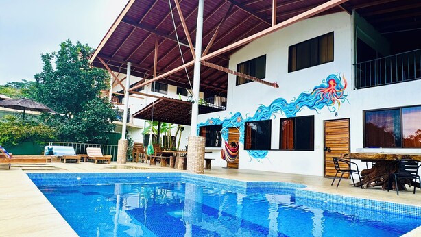 A swimming pool with a tiled deck, a covered seating area, and a building with a mural. - Casa midin 9, Stunning 3bd 2bth condo, GREAT location! (Puerto Carrillo)
