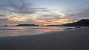 A beach with a calm sea, a clear sky, and a distant shoreline with trees. - Casa midin 9, Stunning 3bd 2bth condo, GREAT location! (Puerto Carrillo)