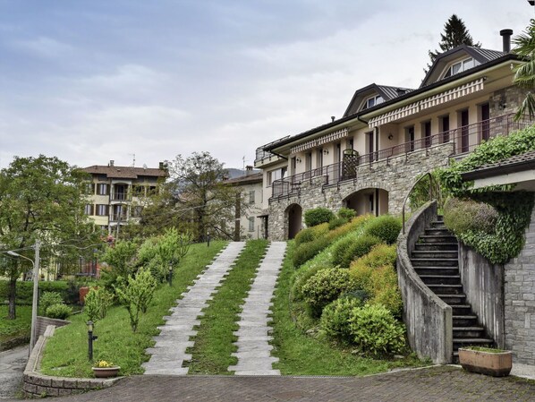 A hillside villa with a stone staircase leading to a balcony, surrounded by lush greenery and a paved pathway. - Wonderful  villa for 4 people with WIFI, TV and terrace (Luino)