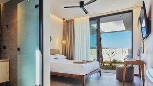 A modern bedroom with a bed, a ceiling fan, a TV, and a view of the outdoors. - Walking distance to Beach, Heated Pool & Rooftop Hot Tub! (Rethymno)