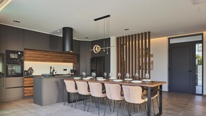 A modern kitchen with a central island, built-in appliances, and a dining area with a long table and chairs. - Walking distance to Beach, Heated Pool & Rooftop Hot Tub! (Rethymno)