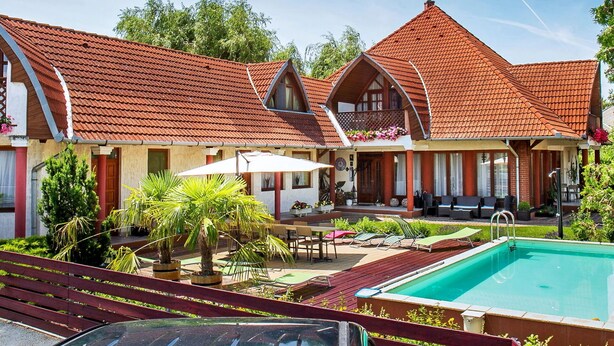A two-story building with a red-tiled roof and a swimming pool.