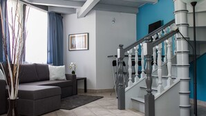 A living room with a grey sofa, a small table, and a vase with branches. There is a staircase with white balusters and a blue wall in the background.