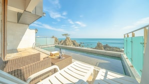 A rooftop pool with a view of the ocean and rocky outcrops, furnished with wicker chairs and a table. - Gyeongju Blue21 Poolvilla Pension (Gyeongju)