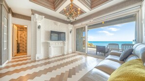 A spacious living room with a fireplace, a television, and a large sliding glass door leading to a balcony with a view of the sea. - Gyeongju Blue21 Poolvilla Pension (Gyeongju)