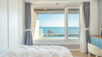 Un dormitorio con un ventanal grande, una cama, un tocador y vista al mar.