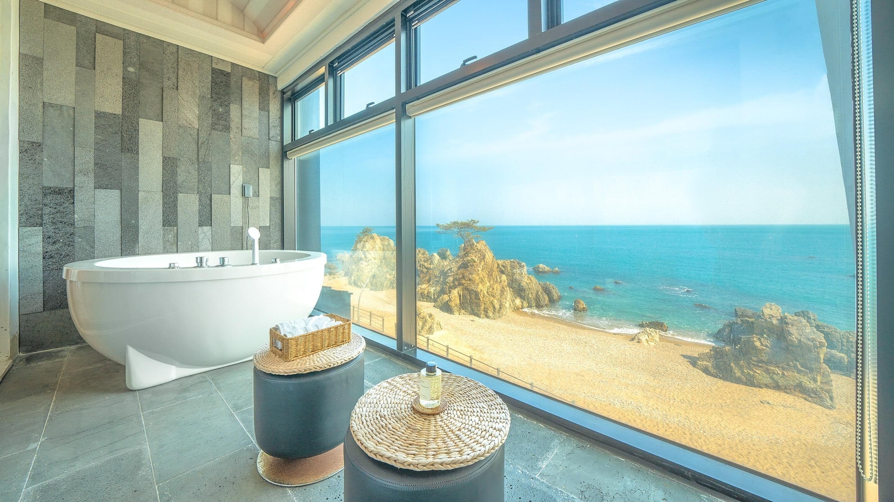 A modern bathroom with a freestanding bathtub, a wicker basket, and a round stool.