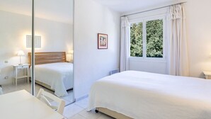 Une chambre d’hôtel avec deux lits, un bureau, une chaise, une fenêtre avec des rideaux et un tableau au mur.