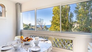 Un coin repas avec une table mise pour le petit-déjeuner, offrant une vue panoramique sur les arbres et la mer.