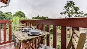 Eine Holzterrasse mit einem für zwei Personen gedecktem Tisch, mit Blick auf einen Garten.