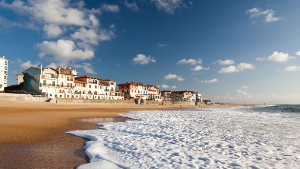 Ein Strand mit einer Reihe bunter Gebäude entlang der Küste, feinem Sand und brechenden Wellen.