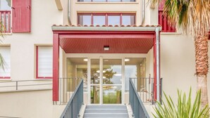 Ein Gebäudeeingang mit rotem Vordach, Glastüren und einer Treppe.