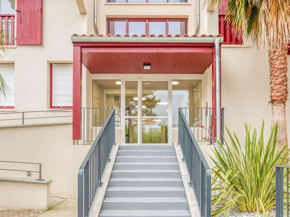 Une entrée d’immeuble avec un auvent rouge, des portes vitrées et un escalier menant à l’étage.