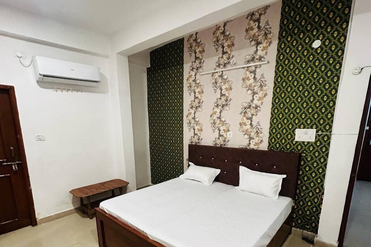 A bedroom with a large bed, a wooden headboard, a small bedside table, and an air conditioning unit on the wall.