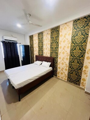 A bedroom with a bed, a ceiling fan, an air conditioning unit, and patterned wallpaper. - GREEN SAPPHIRE INN - BHOPAL (Bhopal)