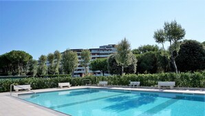 Piscina rectangular con solárium alicatado, rodeada de follaje y bancos.