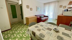 Una habitación con una mesa de comedor, sillas, un sofá, un armario de madera y una puerta verde.