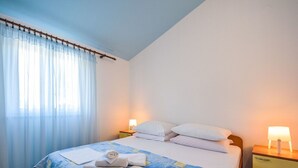 A hotel room with a bed, two bedside tables, a window with curtains, and a nightstand with a lamp.