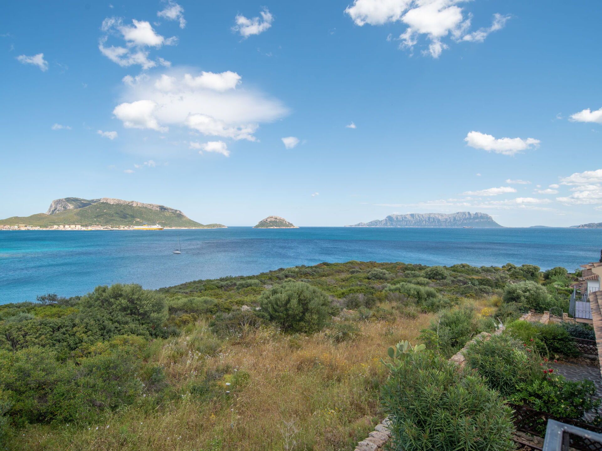 Un paysage côtier offrant une vue dégagée sur la mer, une petite île et une chaîne de montagnes lointaine.