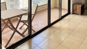 Un balcon avec une porte-fenêtre coulissante, une petite table en bois et une chaise.