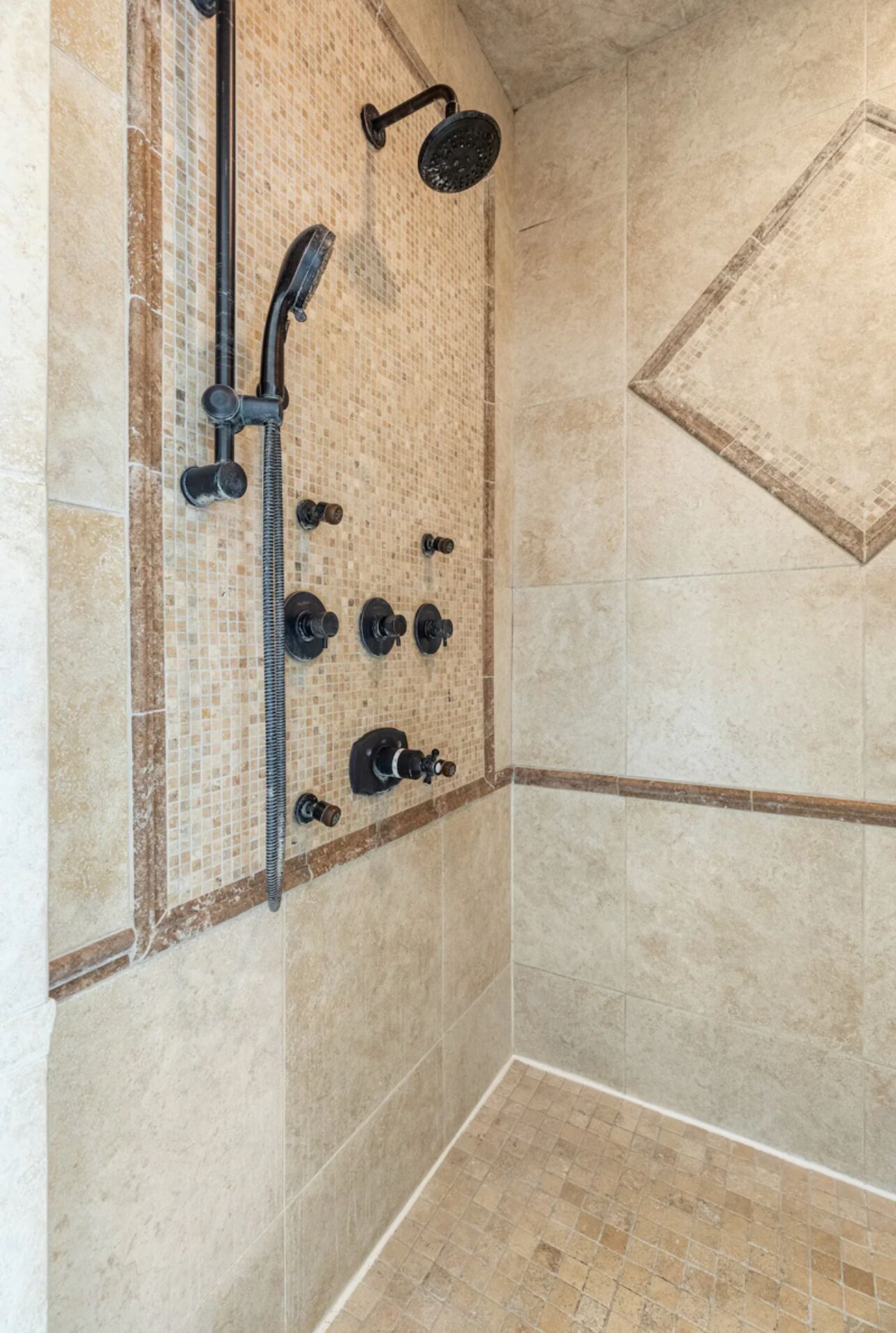A shower with a handheld showerhead, a wall-mounted showerhead, and a control panel with multiple knobs.