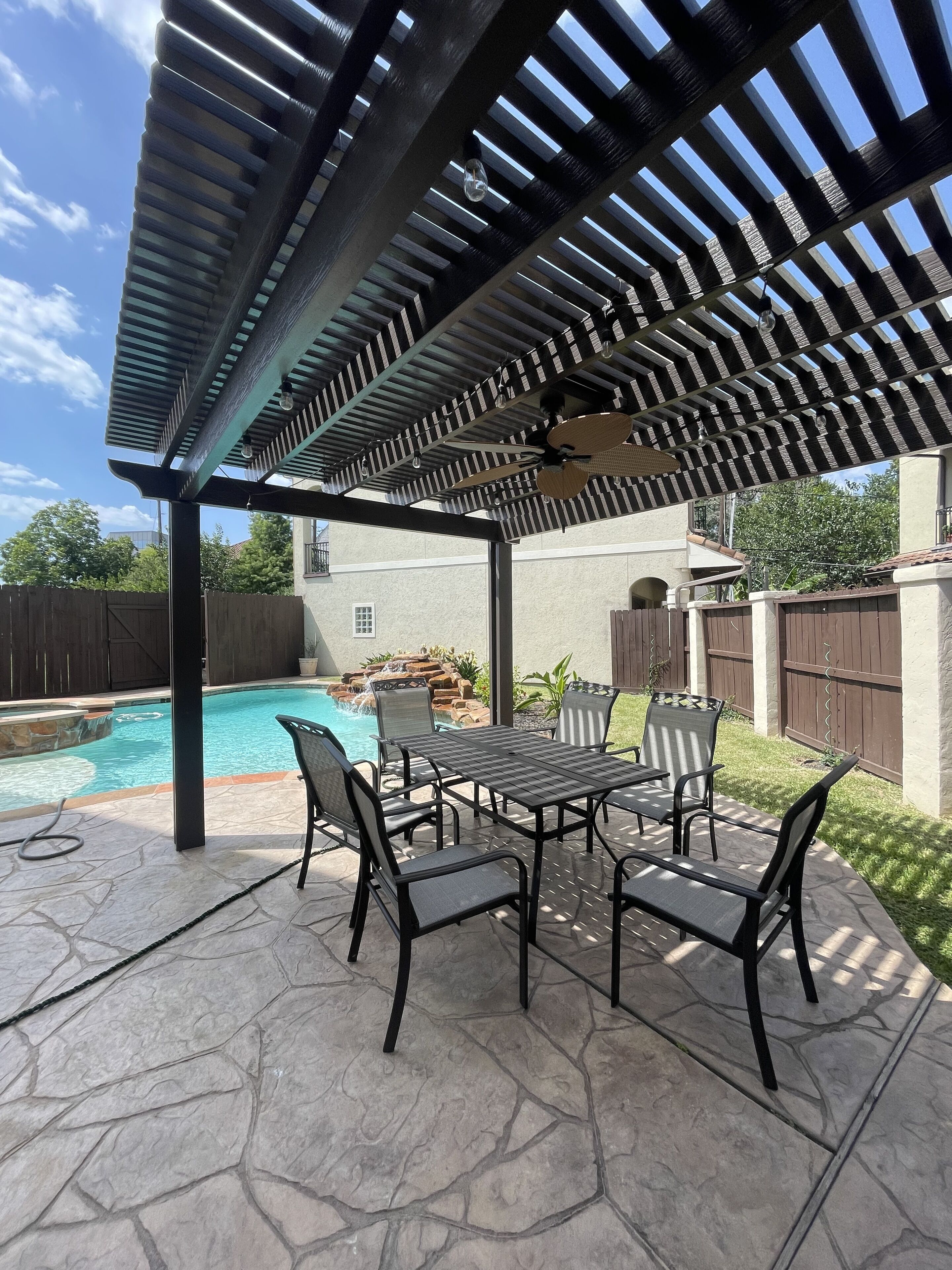 An outdoor patio with a pool, stone flooring, and a pergola with striped awning.