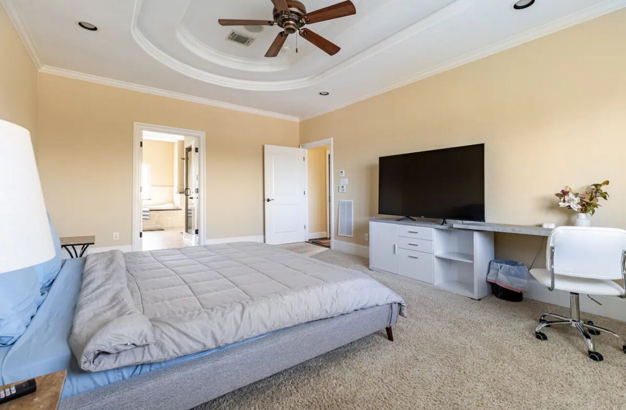 A bedroom with a bed, a desk, a TV, and a ceiling fan.