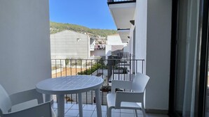 Een balkon met een ronde tafel en twee stoelen, met uitzicht op een woonwijk met huizen en een heuvel.