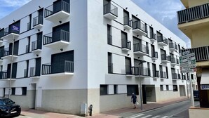 Een modern meerlaags gebouw met balkons, een voetgangersoversteekplaats en een straat met een geparkeerde auto.