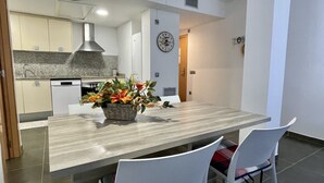 Een moderne keuken met een granieten aanrecht, een roestvrijstalen afzuigkap en een eethoek met een houten tafel en witte stoelen.