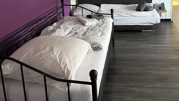 A hotel room with two beds, a purple wall, and a wooden floor. - Red Dot Apartments (Kamen)