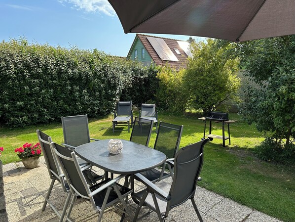 An outdoor patio with a round table and chairs, a grill, and a large umbrella.