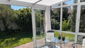A conservatory with a glass table, chairs, and a view of a garden. - 3 bedroom accommodation in Julianadorp aan Zee (Julianadorp aan Zee)