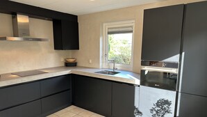 Una cocina moderna con armarios negros, una campana de acero inoxidable, una ventana con vistas a zonas verdes y suelo de baldosas.