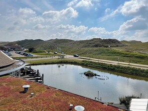 A lakeside hotel with a view of the lake, a parking area, and a road with vehicles.