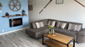 Una sala moderna con un sofá modular, una mesa de centro de madera, un televisor montado y objetos decorativos como una rueda de barco y bates de béisbol.