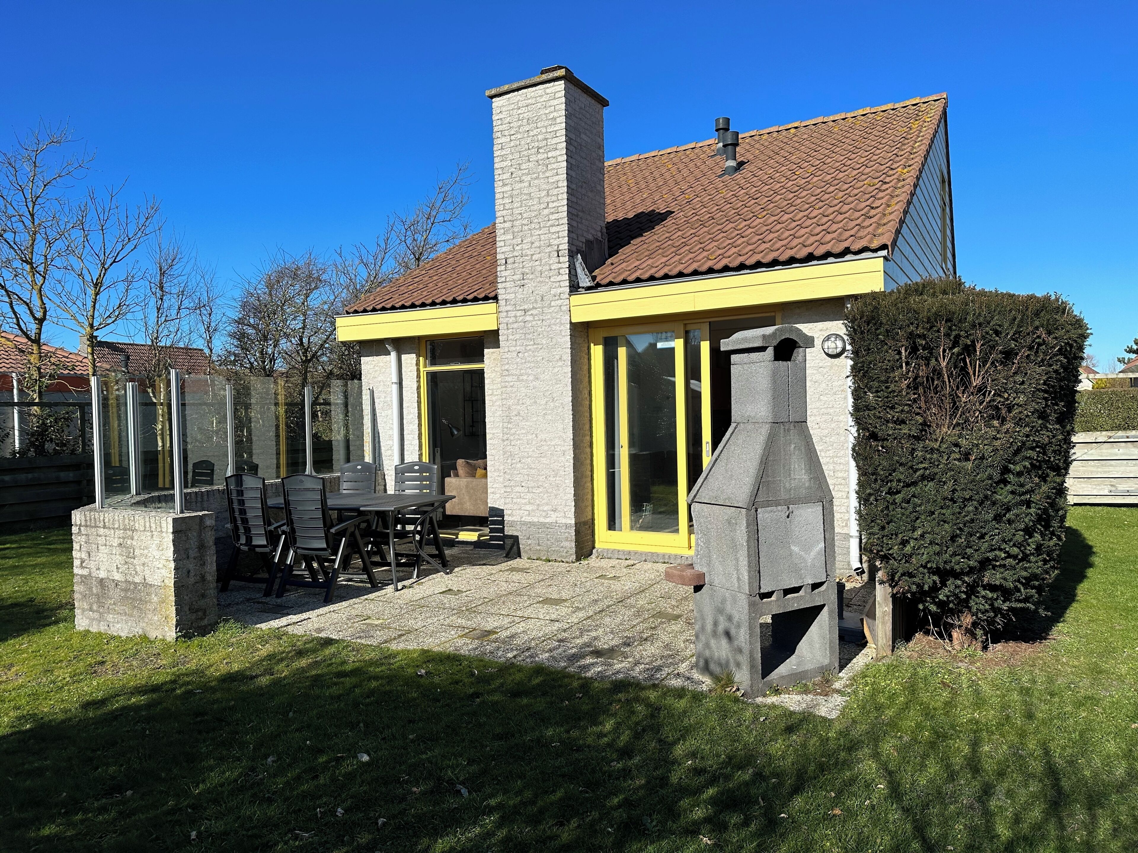 Una casa con chimenea de piedra, puerta con marco amarillo y un patio con mesa y sillas.