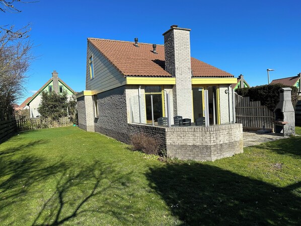 A two-story house with a stone facade, a tiled roof, and a small porch with chairs.