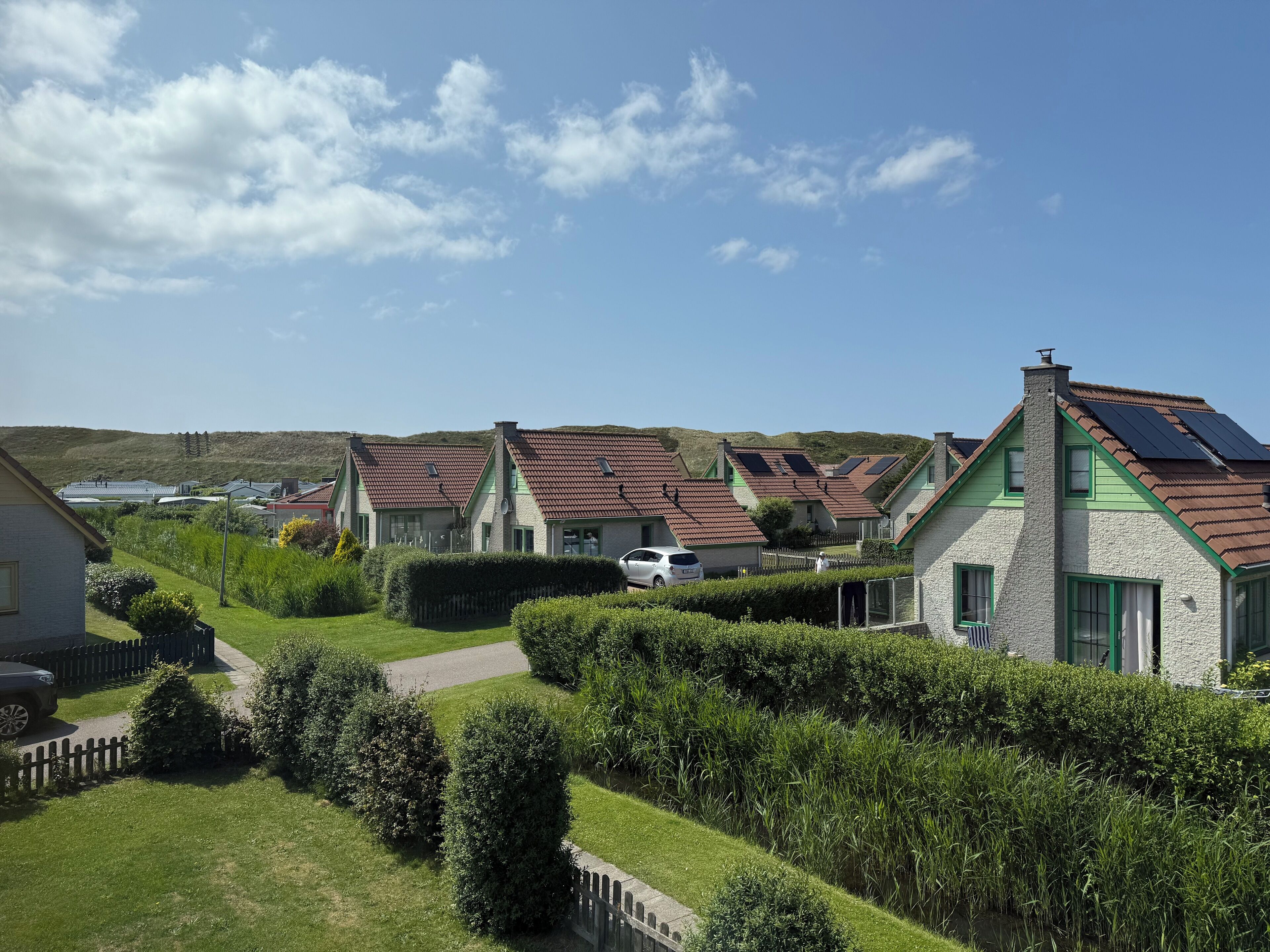 A row of houses with sloped roofs, likely equipped with solar panels, set in a green, hilly area.